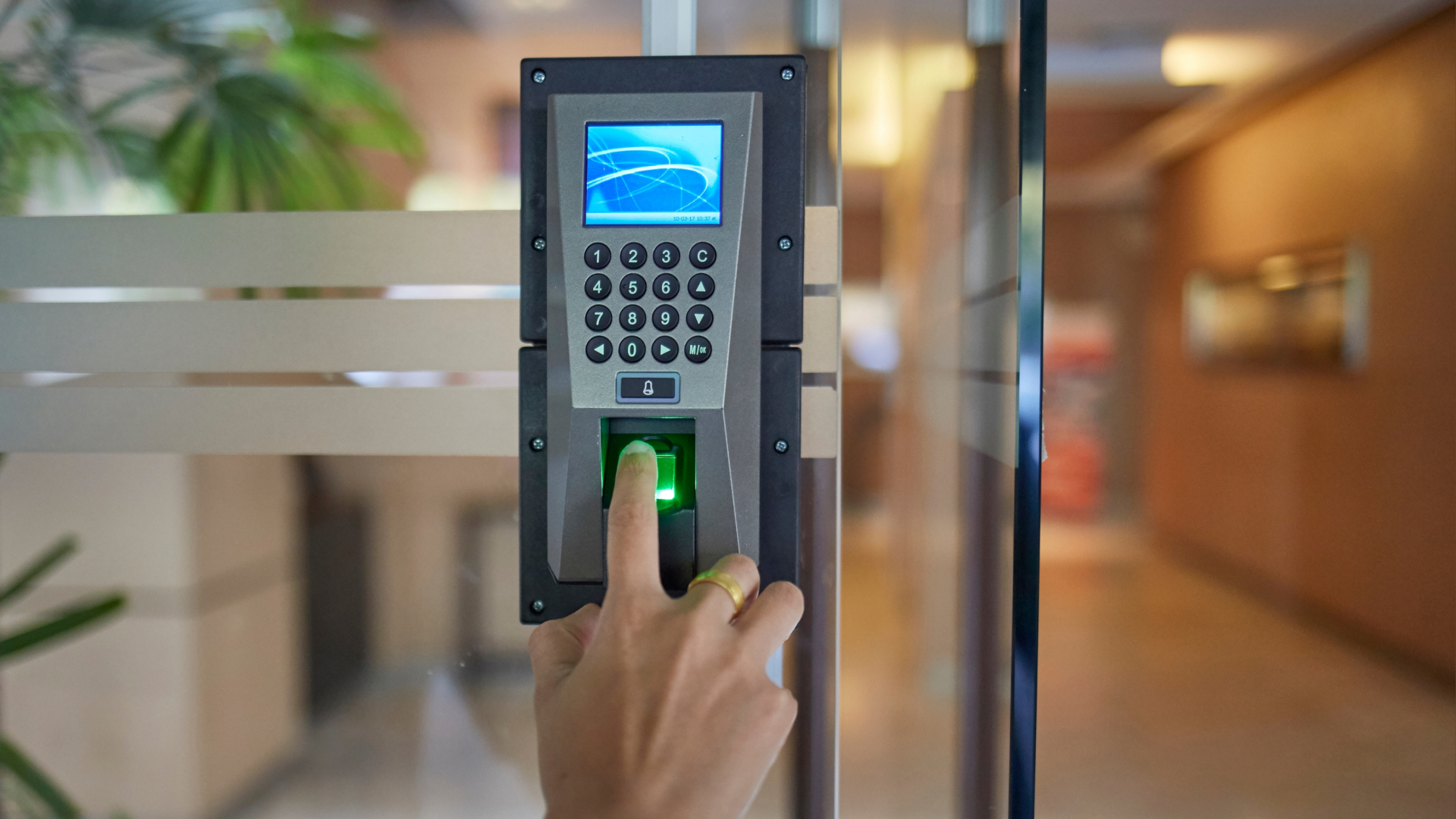 Close-up of a finger pressing a fingerprint scanner on a wall-mounted time clock.