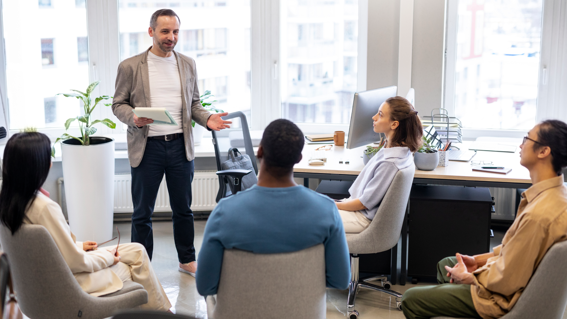 Man standing and addressing a seated group of colleagues in an office meeting.