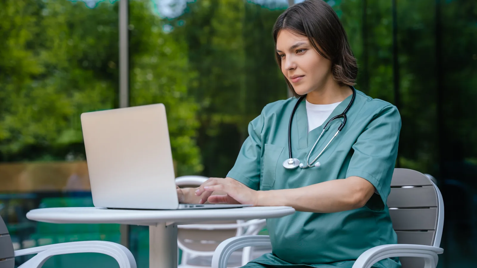  A nurse in green scrubs works on a laptop outdoors, illustrating various 7 shift patterns in healthcare.