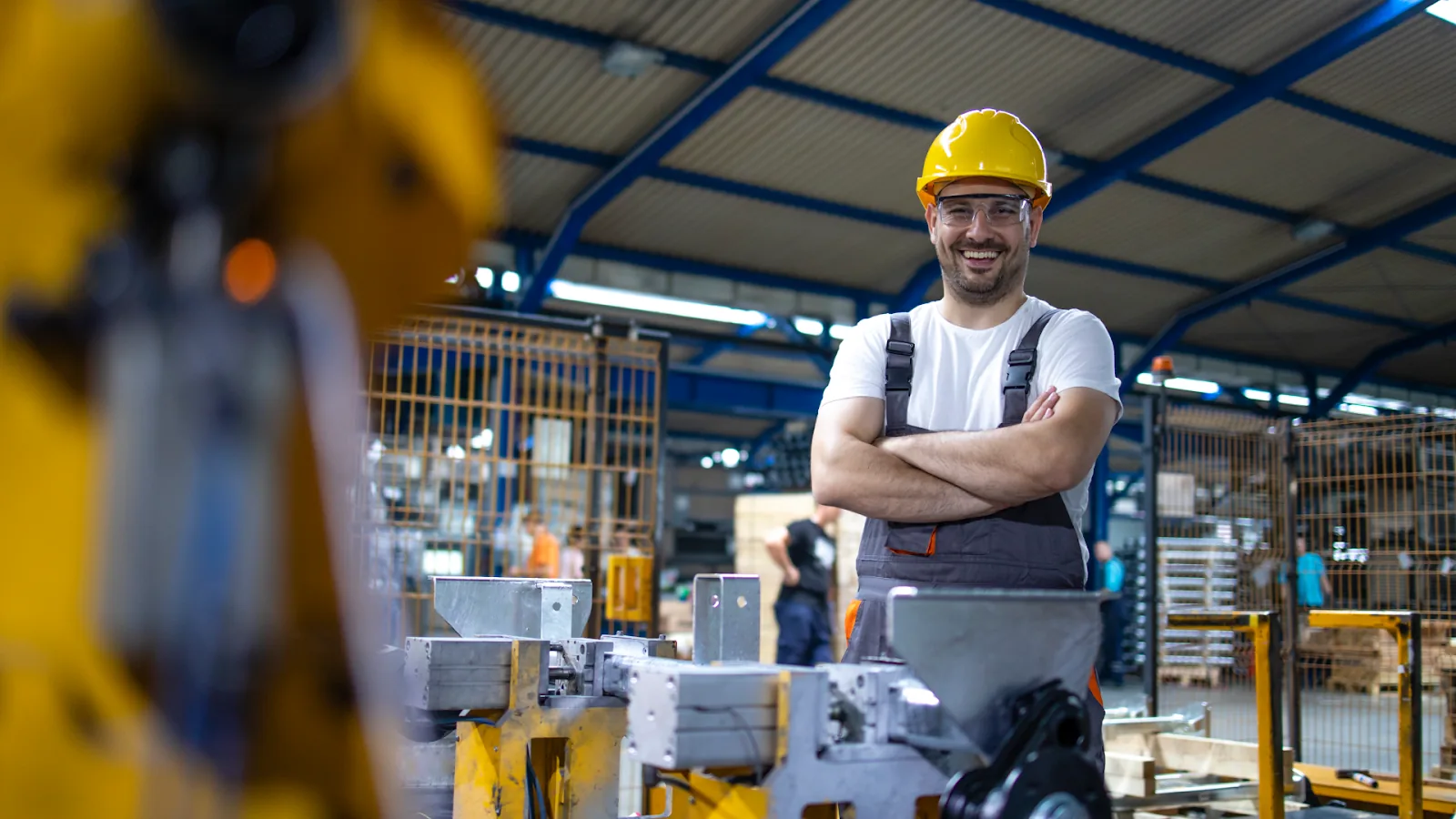 A smiling worker in a yellow hard hat in a warehouse setting.