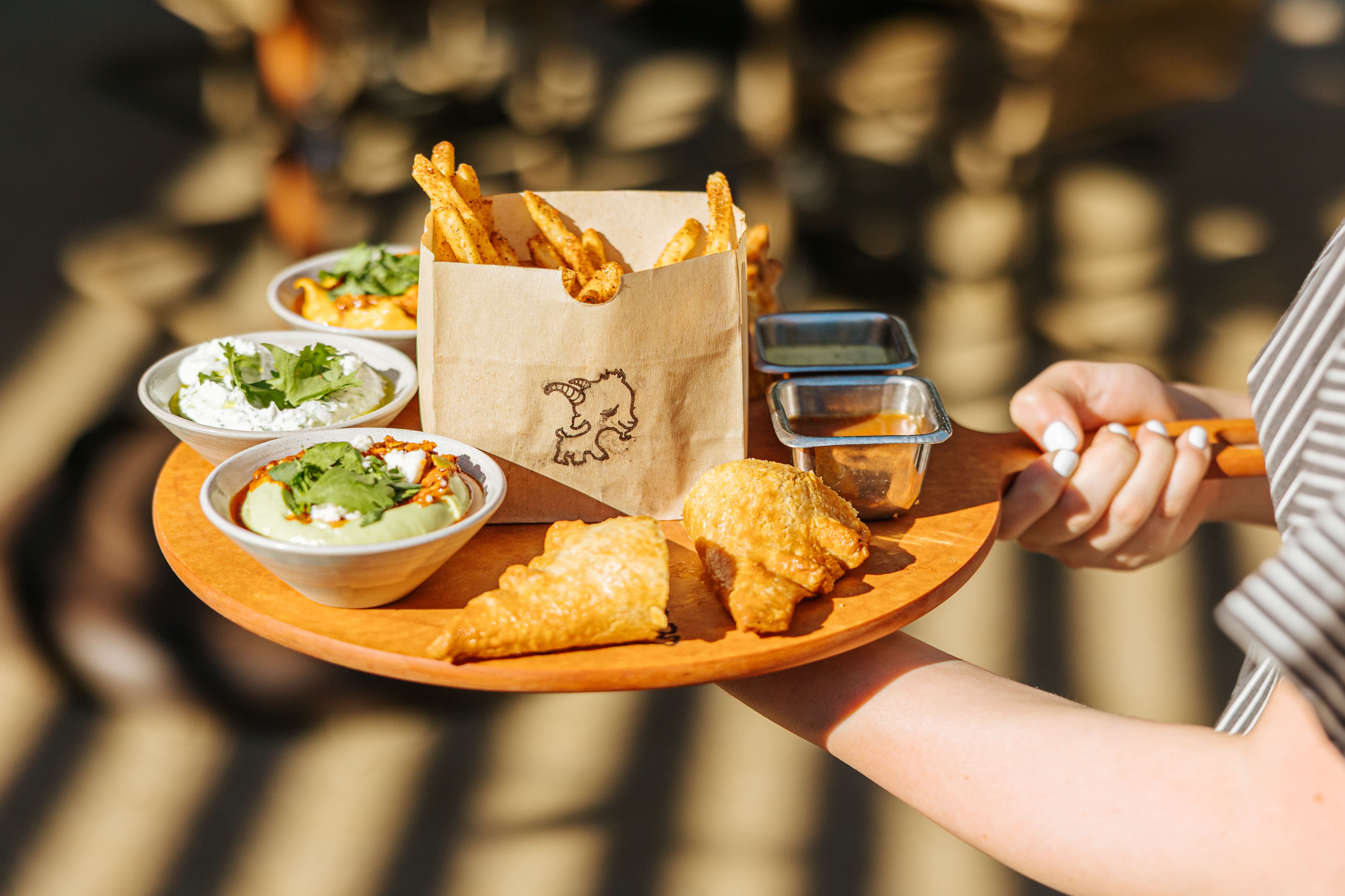 Server holding an Alley Goat grazing board with seasoned fries, dips, sauces, and fried pastries.