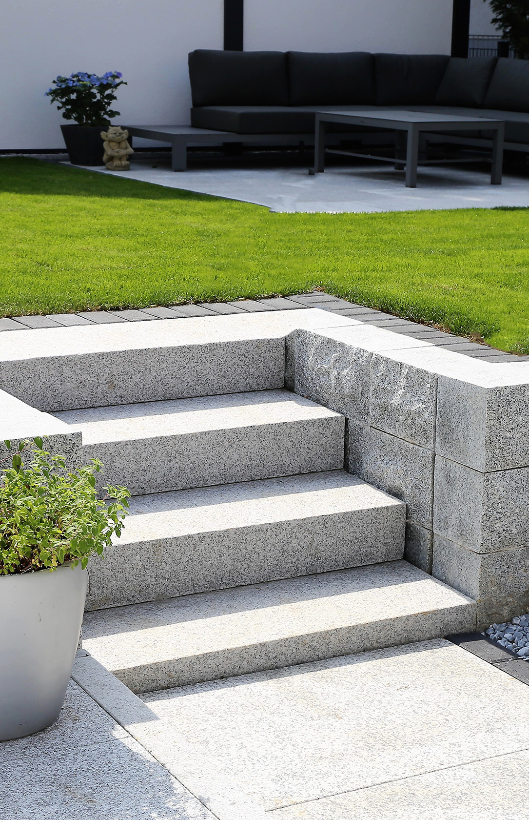 Stein-Treppen im Garten, hellgrauer Granit. 4 Stufen führen zu einer mit Rasen umrandeten Terrasse. 