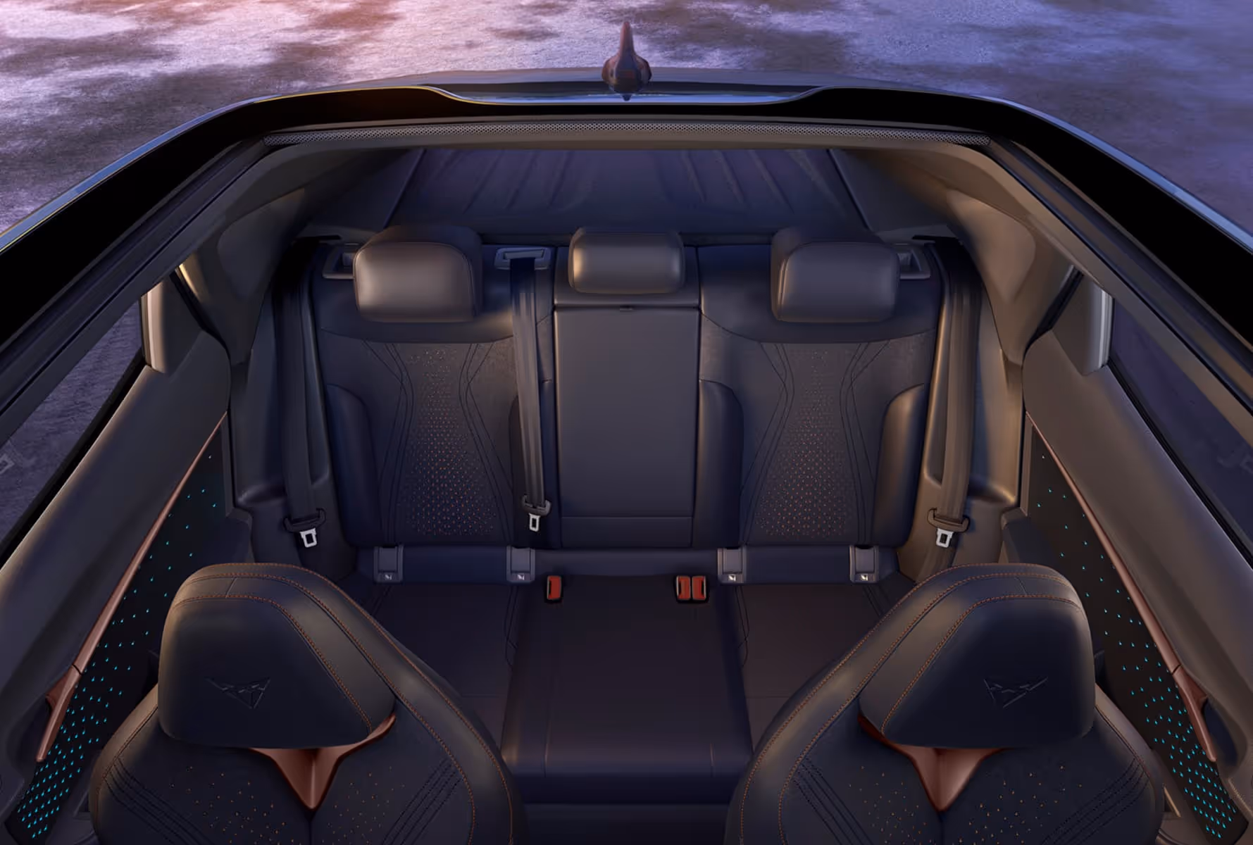 Rear interior view of a car showing three black leather seats with headrests and seat belts, and two front seats with orange stitching and a logo on the headrests.