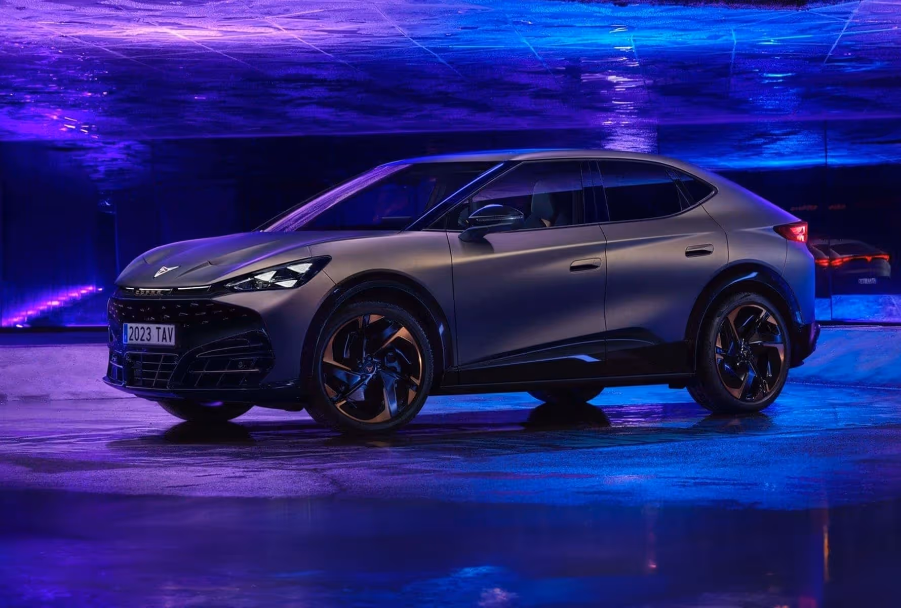 Side view of a matte gray futuristic SUV parked indoors with purple and blue lighting reflections.