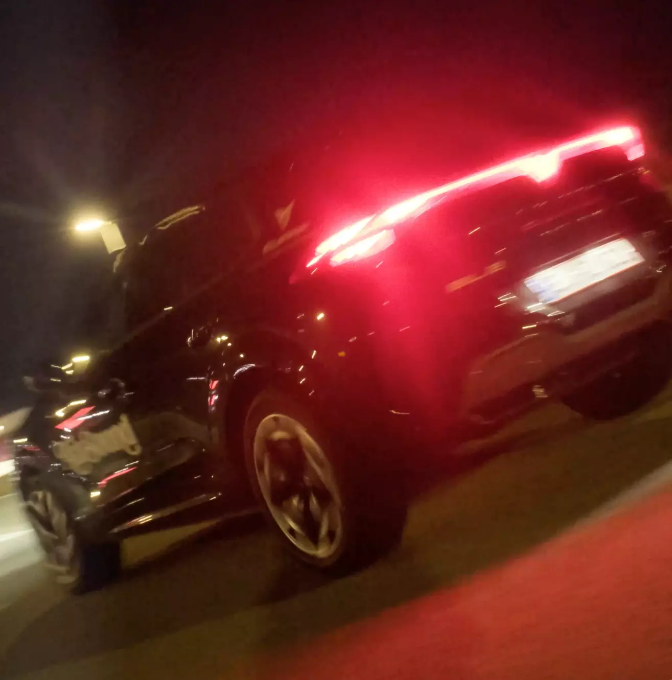 Black car with illuminated red tail lights at night, angled from rear side.