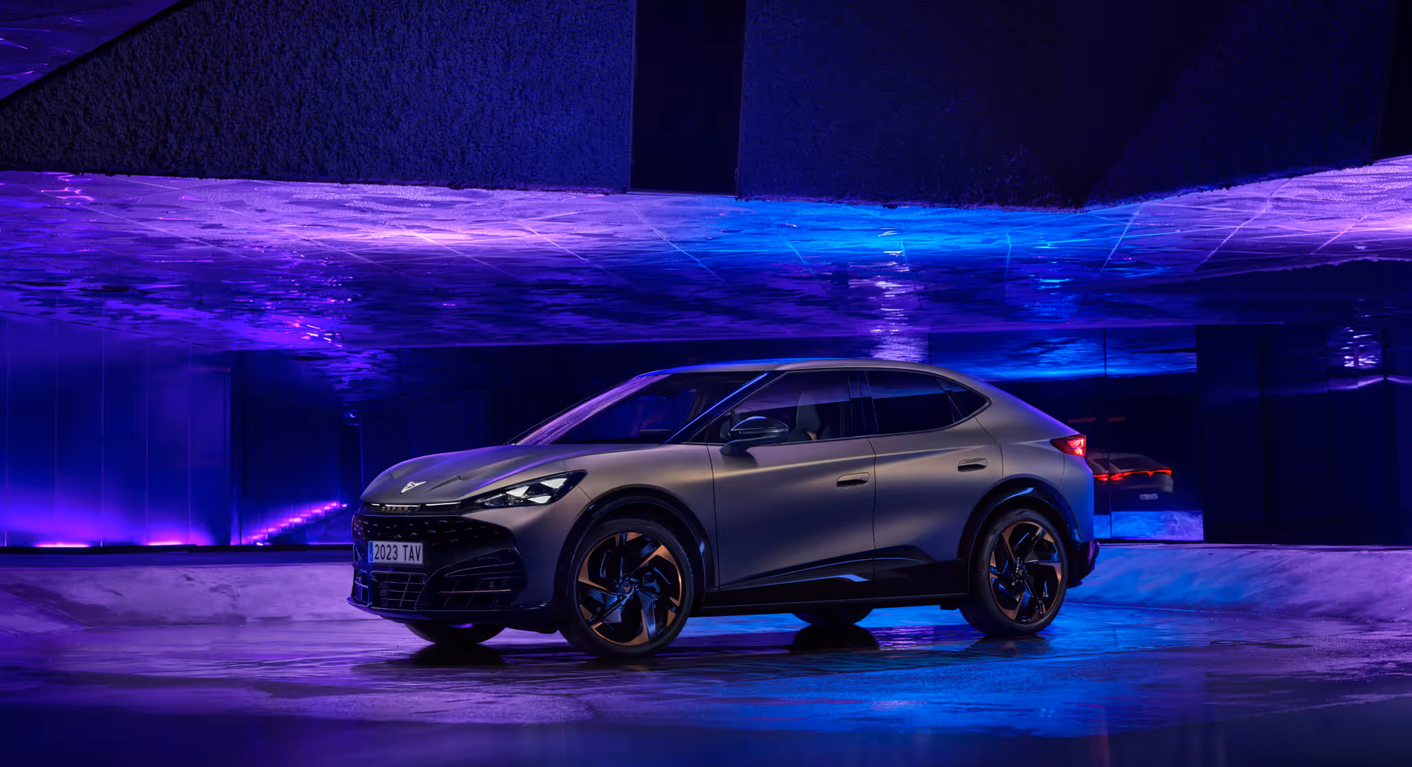Side view of a gray sleek modern car parked indoors under purple and blue ambient lighting.