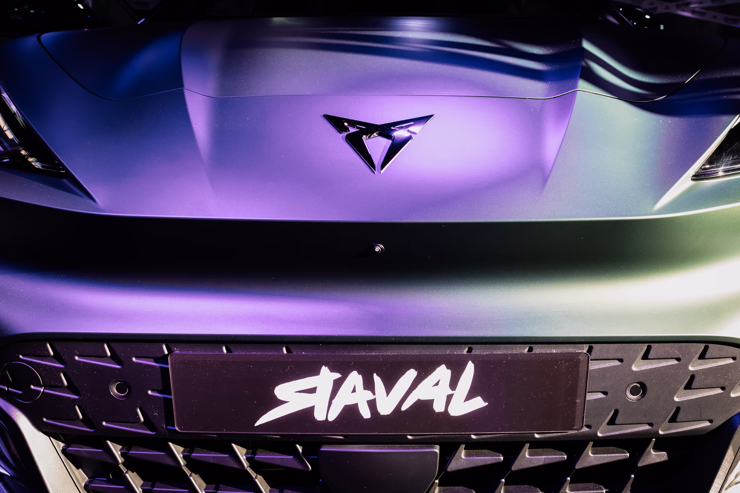 Interior view of car door panel with textured trim, illuminated small arrow patterns, window control button, and side mirror.