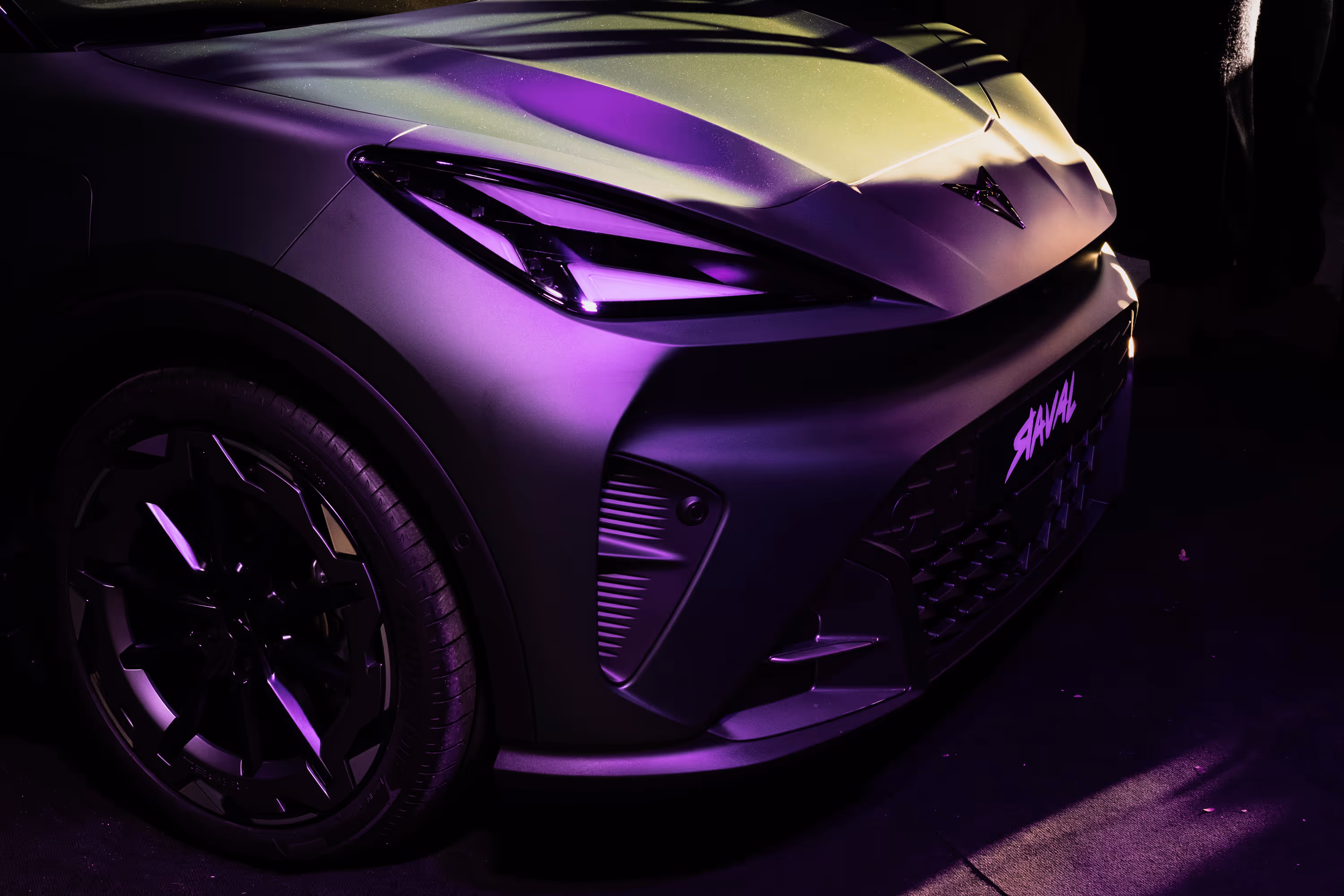 Interior close-up of two black leather car seats with orange stitching and a logo on the headrests at dusk.