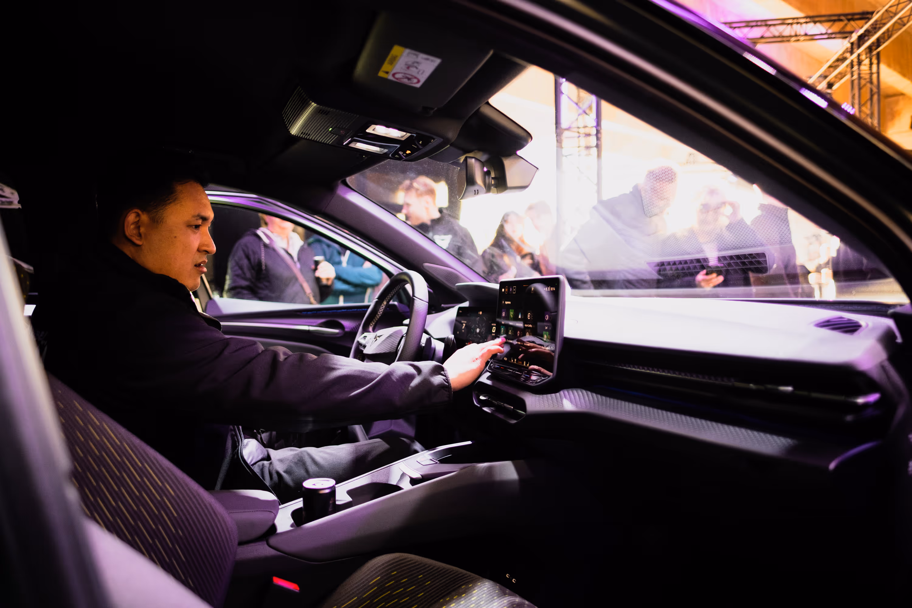 Interior view of a modern car cockpit at dusk with a digital steering wheel, central touchscreen display, and ambient lighting.