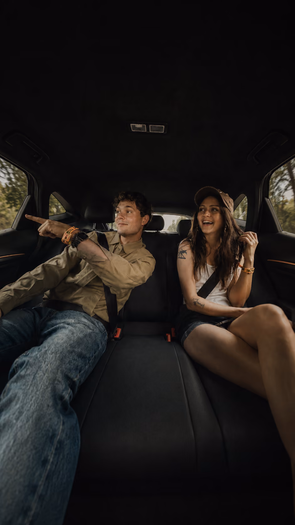 Man pointing excitedly out car window while woman next to him laughs inside backseat of car.