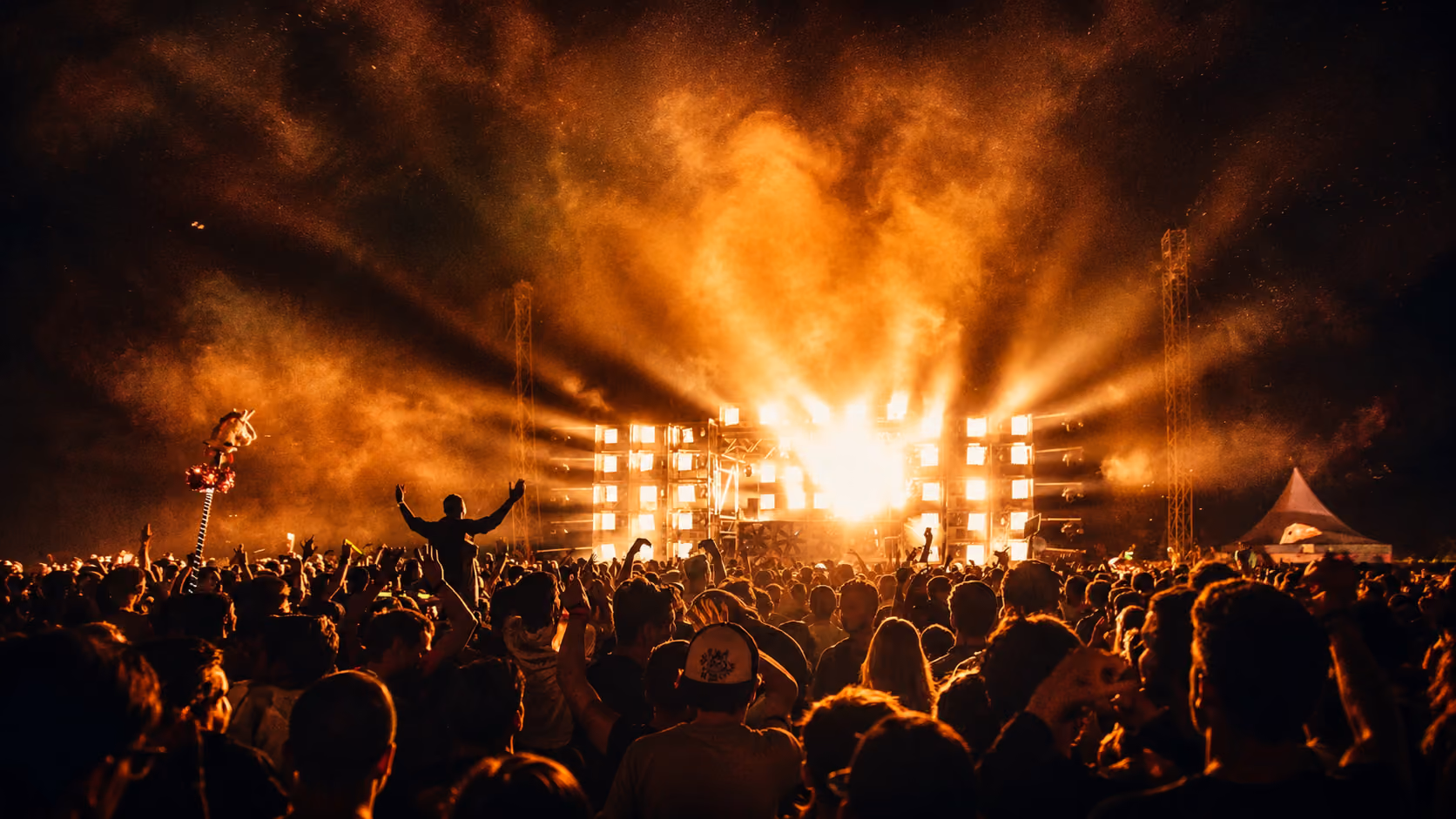 Large crowd at a night concert with bright orange stage lights and smoke effects.