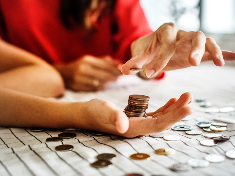 Manos contando y apilando monedas sobre una mesa con un mantel a cuadros.