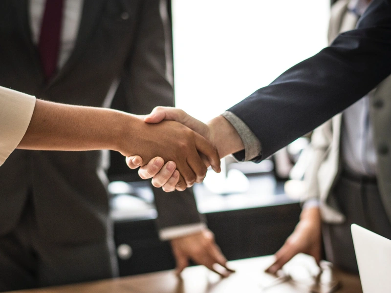 Dos personas vestidas de negocios dándose la mano sobre un escritorio.