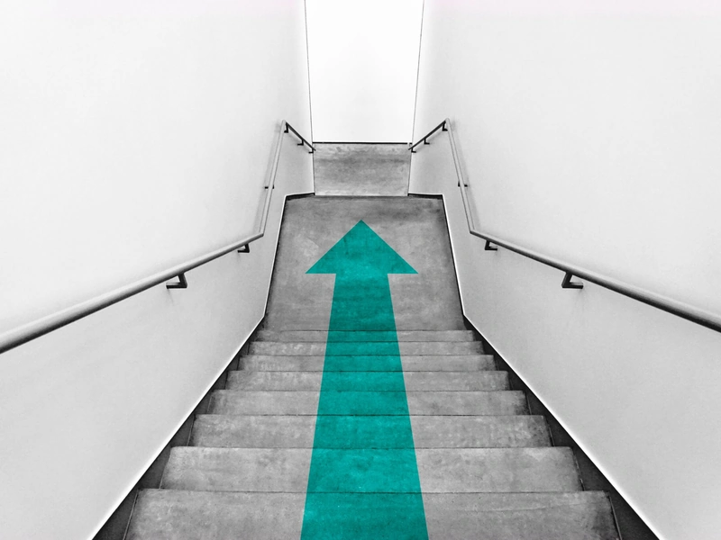 Escalera descendente con una flecha de color verde azulado brillante que apunta hacia arriba en los escalones.