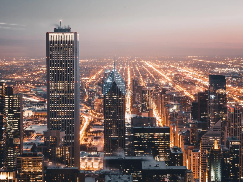 Horizonte de la ciudad al anochecer con edificios iluminados y calles que se extienden en la distancia.