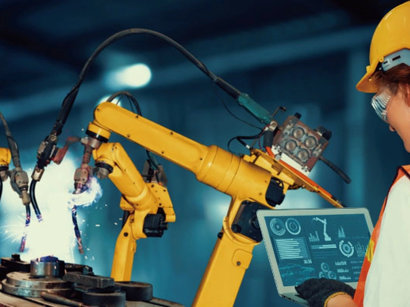 Brazos robóticos industriales que trabajan en una máquina con una persona con equipo de protección.