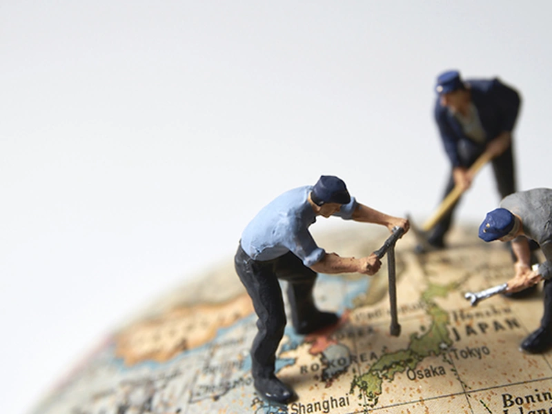 Figuras en miniatura de trabajadores de pie sobre un globo terráqueo, usando herramientas para cavar en el mapa.