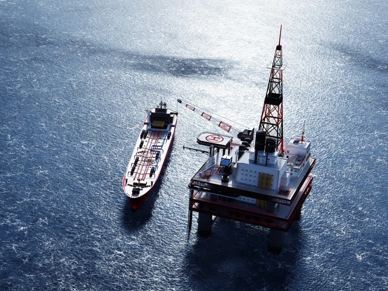 Plataforma petrolífera en alta mar con grúa, junto a un gran buque cisterna en aguas tranquilas y azules.
