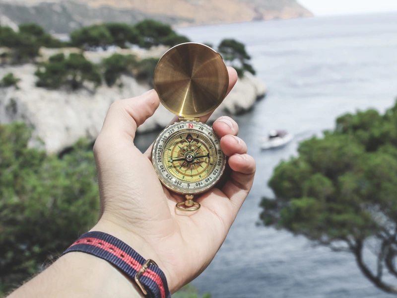 Una mano que sostiene una brújula vintage con el mar y los acantilados verdes de fondo.