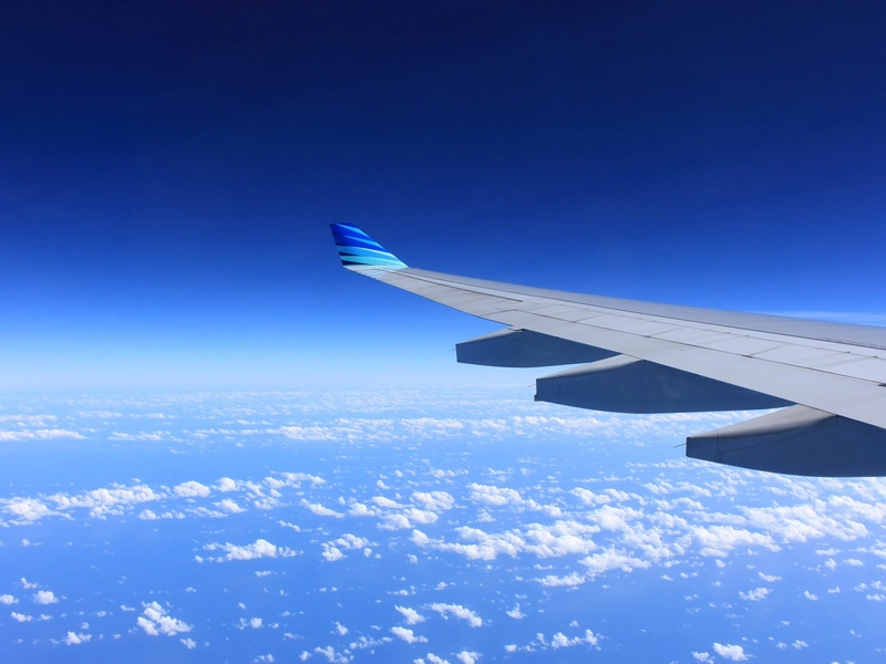 Vista del ala del avión con un cielo azul claro y nubes dispersas en la parte inferior.