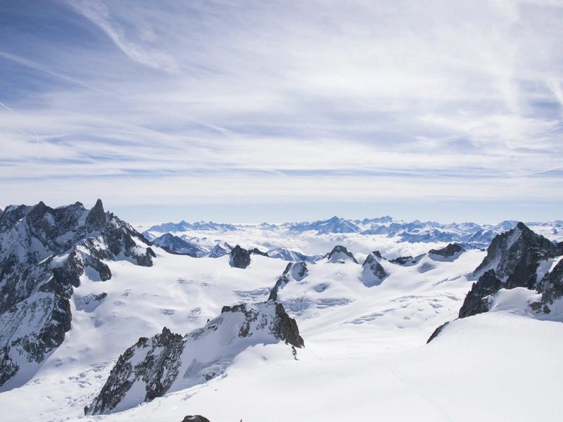 Cordillera cubierta de nieve bajo un cielo nublado con picos distantes visibles en el horizonte.