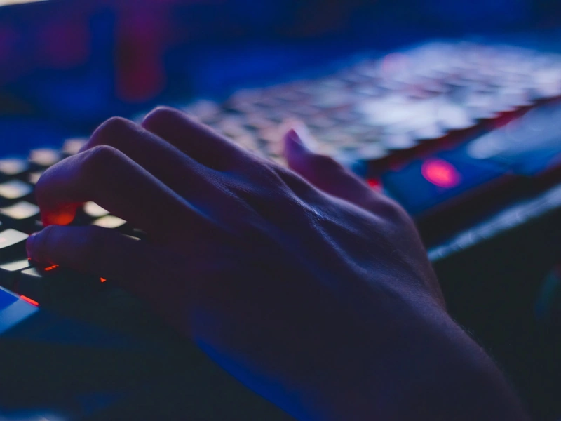 Una mano escribiendo en un teclado retroiluminado en un entorno oscuro con iluminación azul y roja.