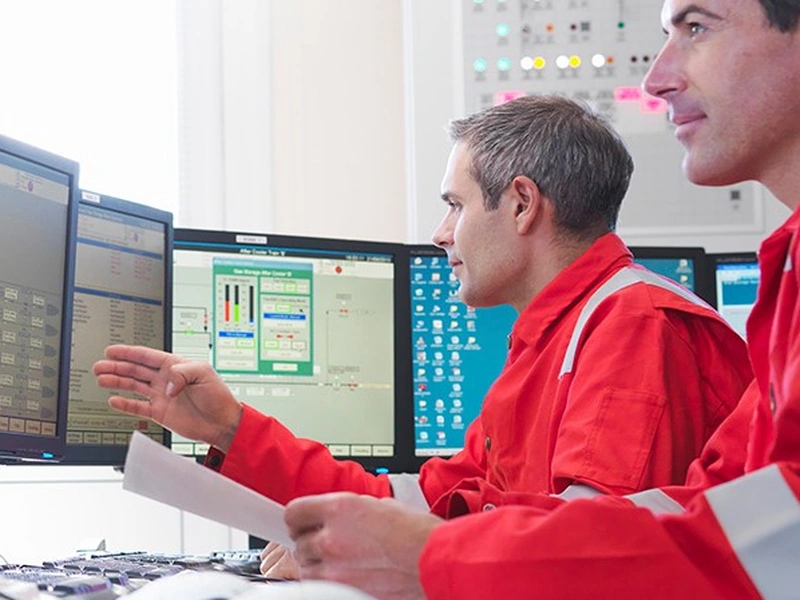 Dos trabajadores con uniformes rojos se centran en varias pantallas de ordenador.