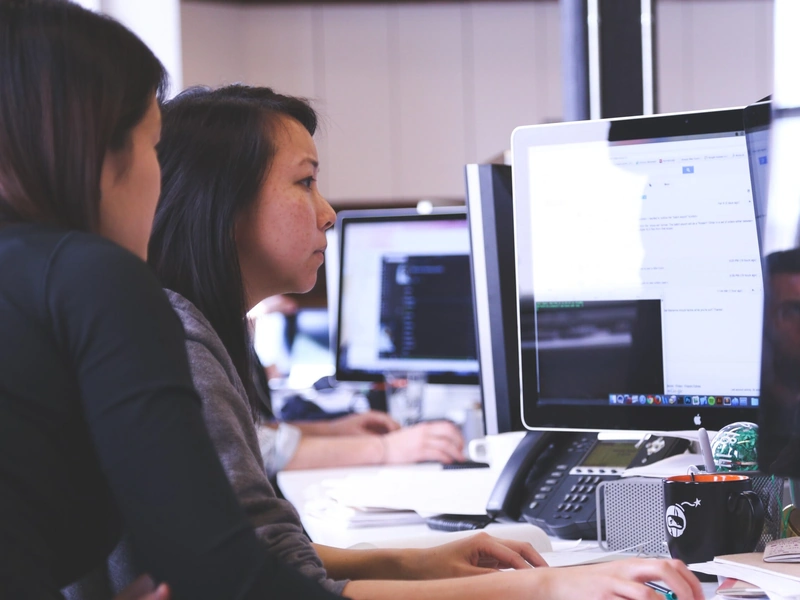 Dos personas trabajando intensamente frente a la pantalla de una computadora en un entorno de oficina.
