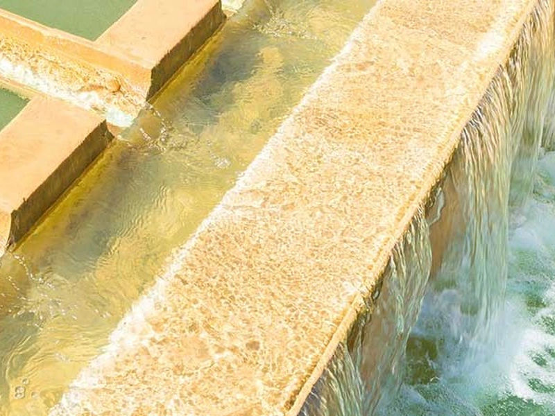 Primer plano del agua que fluye por los bordes de una fuente de piedra escalonada.