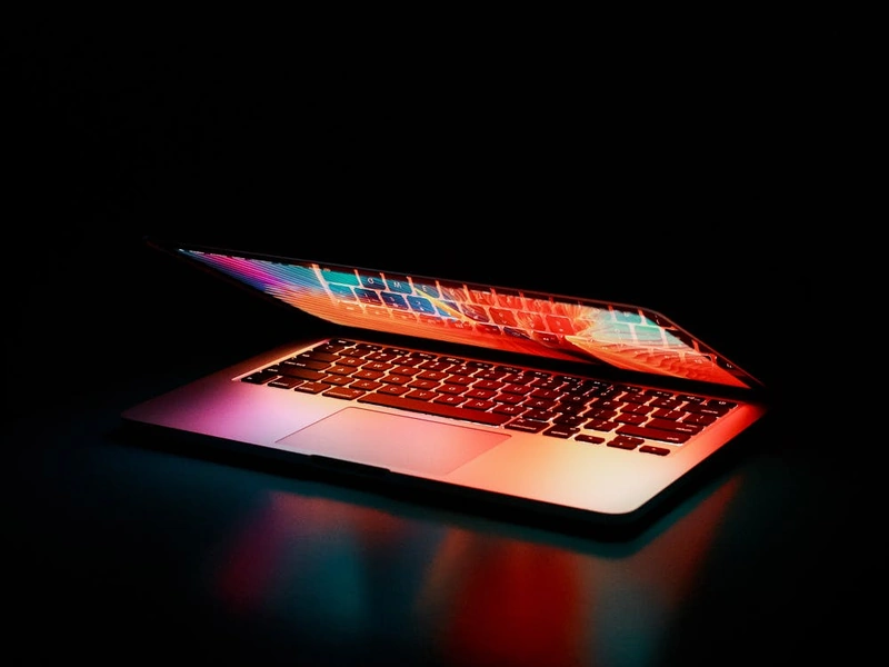 Un portátil parcialmente abierto con una pantalla y un teclado coloridos e iluminados.