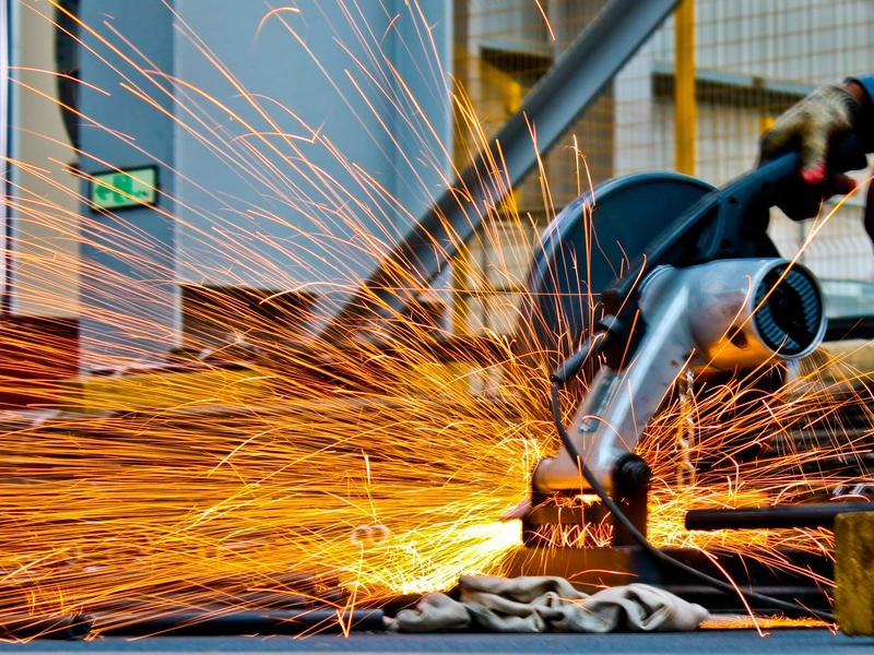 Persona que usa una sierra circular, creando chispas brillantes en un entorno industrial.
