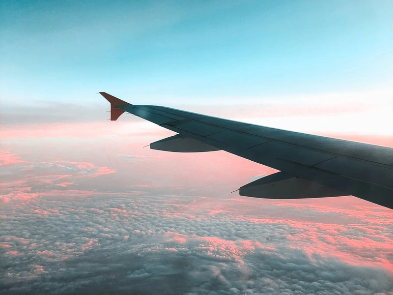 Ala de un avión por encima de las nubes durante una puesta de sol rosa y azul.