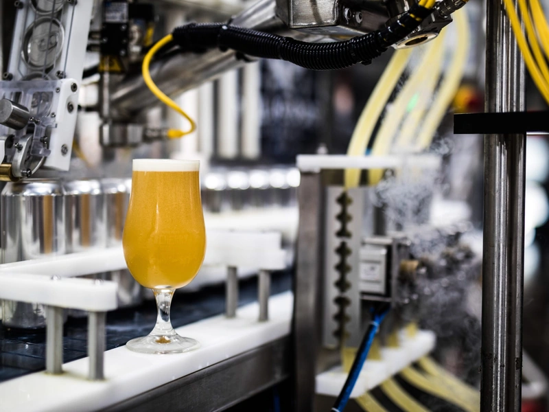Un vaso de cerveza artesanal con una cabeza espumosa se encuentra en una cinta transportadora en una cervecería.