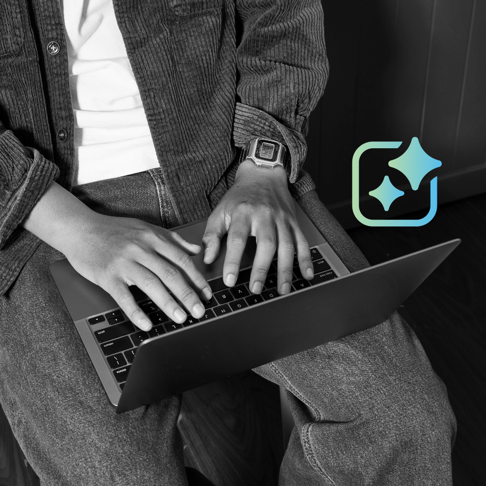 A man sits with a laptop on his lap an AI icon in blue and green gradient is next to him.