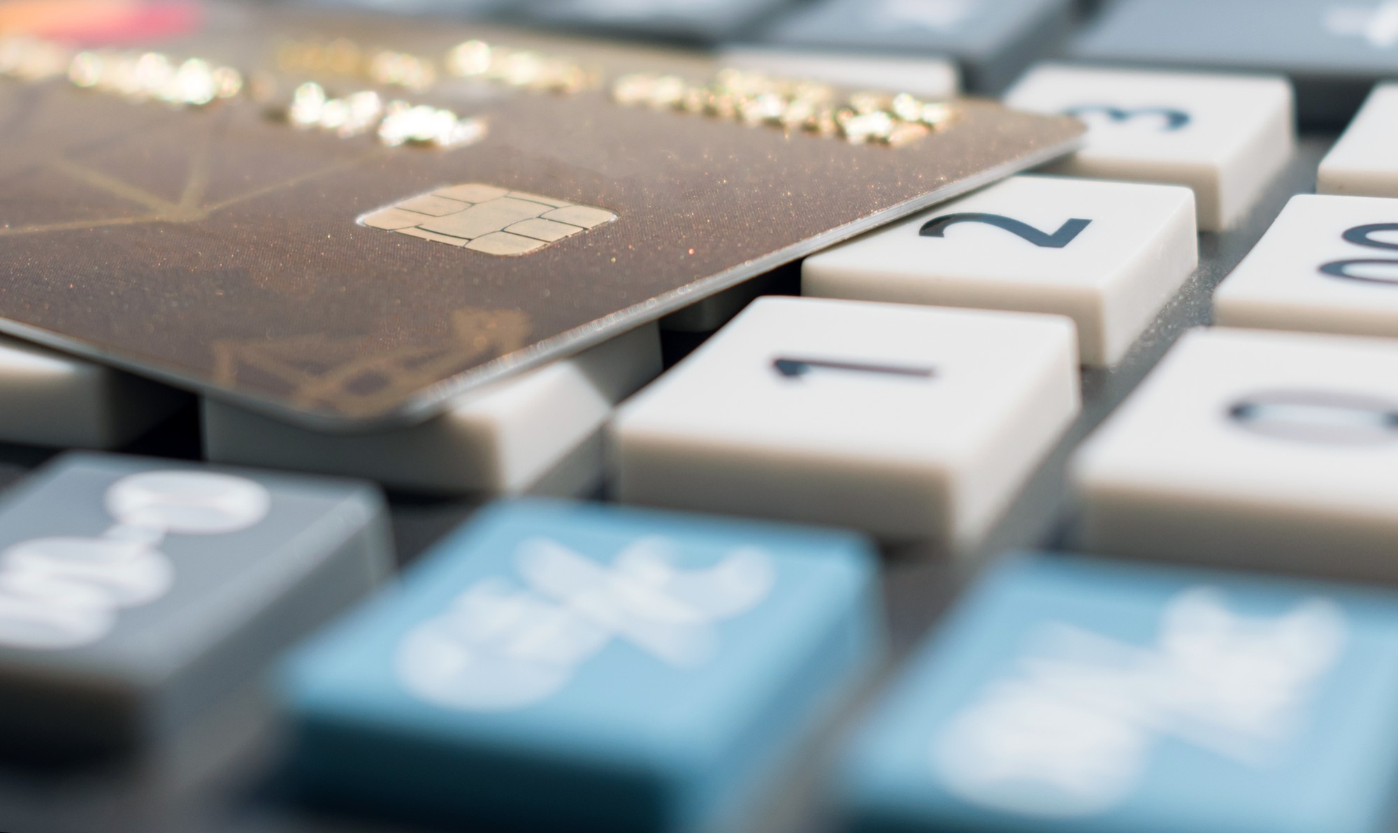 Brązowa karta kredytowa leżąca na klawiaturze kalkulatora z białymi i niebieskimi klawiszami.