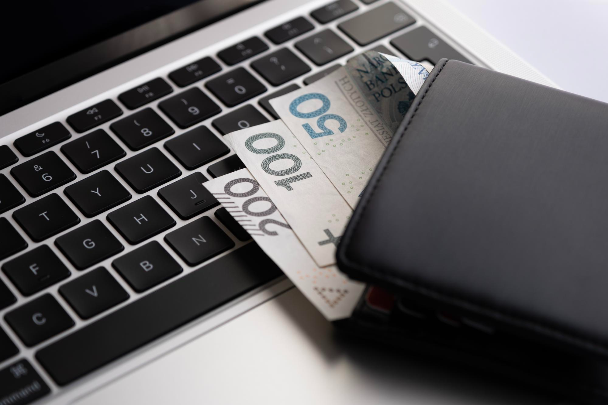 Młoda kobieta z blond włosami i okularami czyta dokument przy biurku z komputerem.