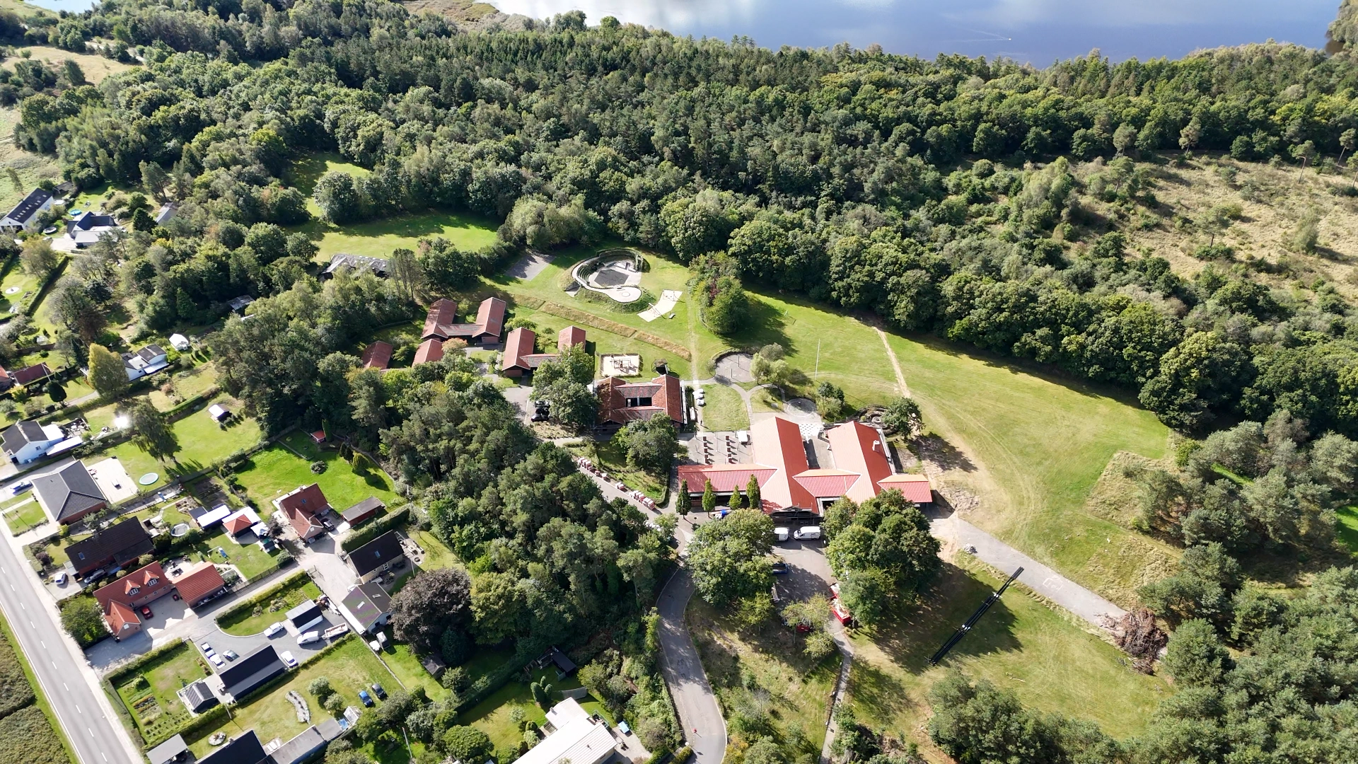 Luftfoto af et forstadsområde med boligbyggerier, åbne marker og veje.