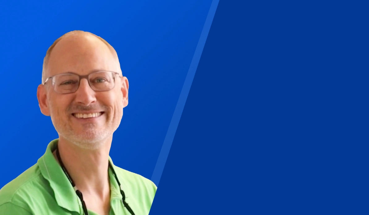 Lächelnder Mann mit Brille und grünem Hemd vor blauem Hintergrund.