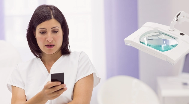 Frau in weißer medizinischer Kleidung schaut auf ihr Smartphone in einem hellen Behandlungsraum.