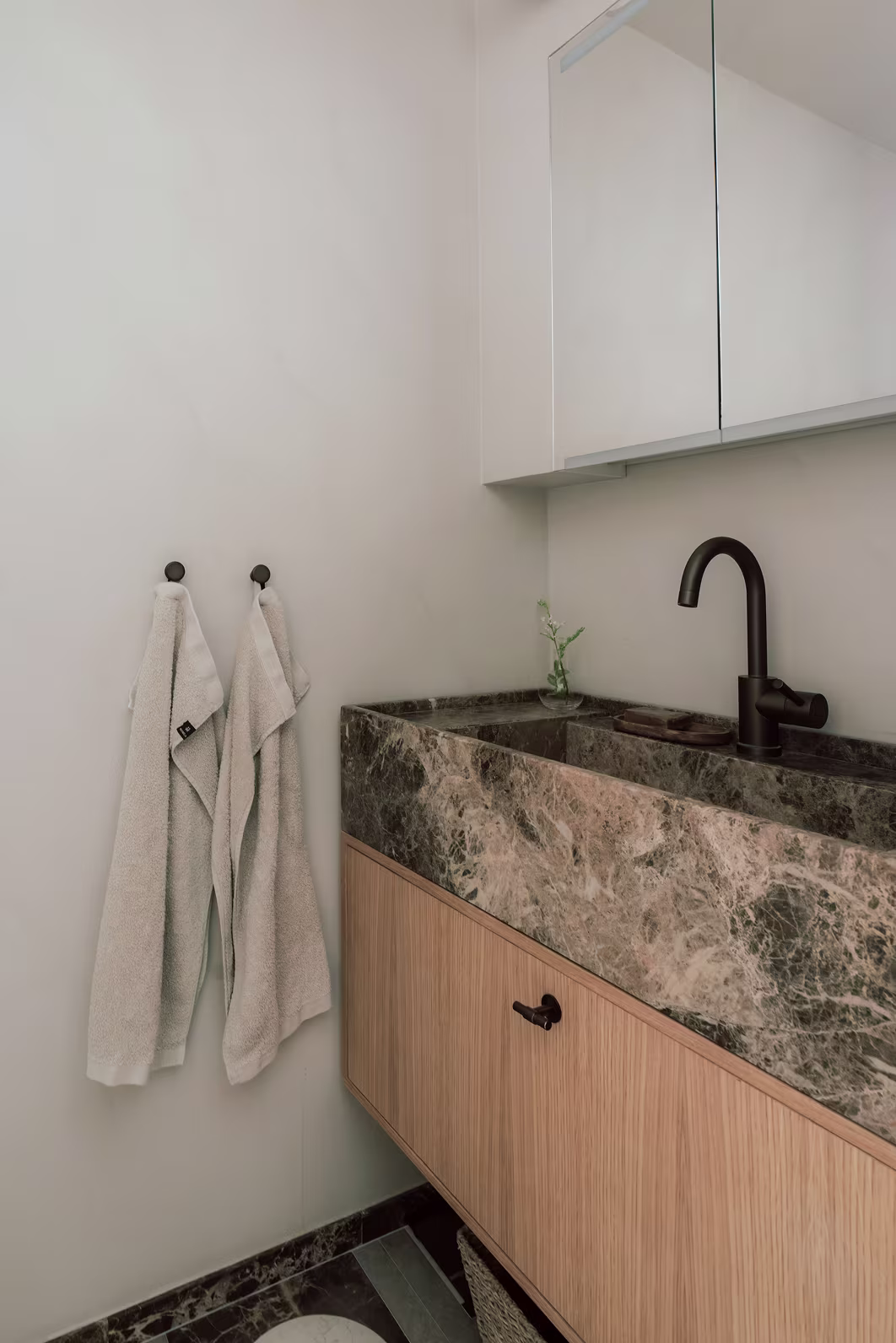 Badrum renoverat av Studio MW med brun och vit  natursten, ljus träkommod och brun blandare i modern inredningsarkitektur.