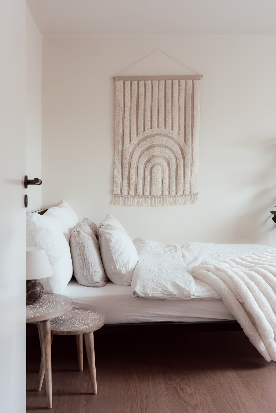 Sovrum i beige toner med trädetaljer, textilier och vägglampor i mjuk, lugn design.