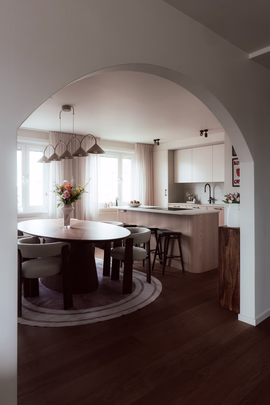 Modern matplats och kök med runt matbord, varma träslag och valv designat av inredningsarkitekt.