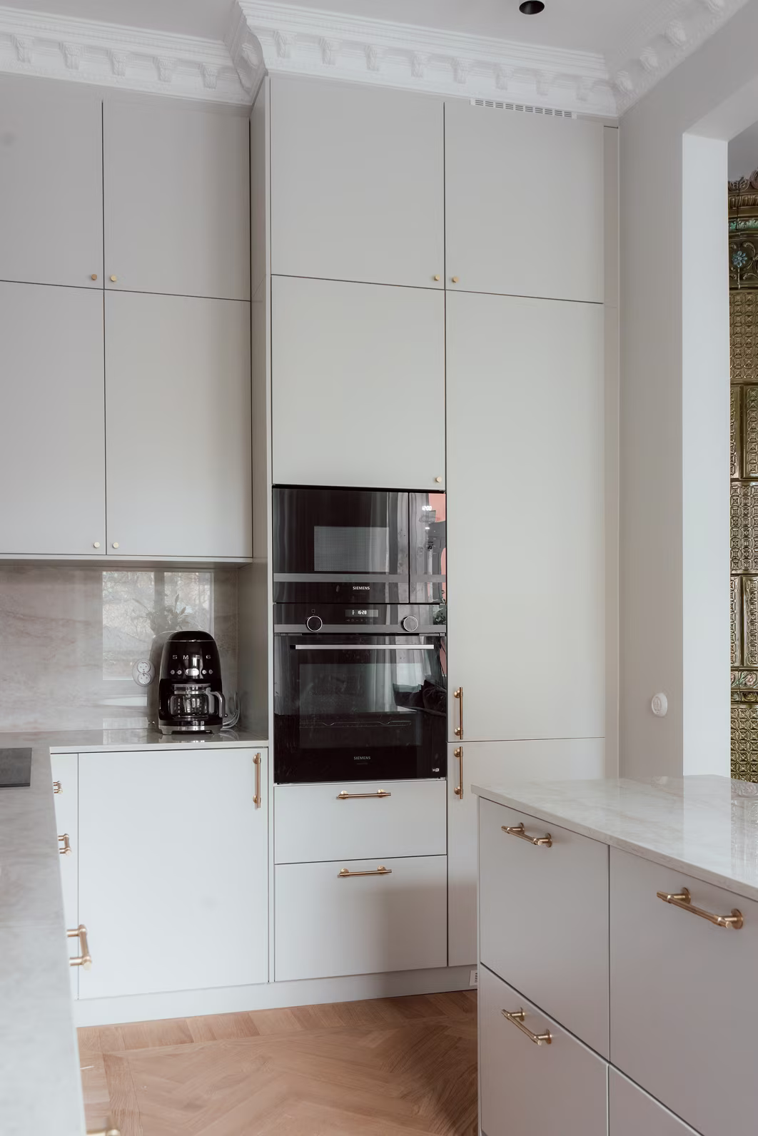 Platsbyggt kök med höga skåp, integrerade vitvaror och tidstypisk elegans i sekelskiftsmiljö.