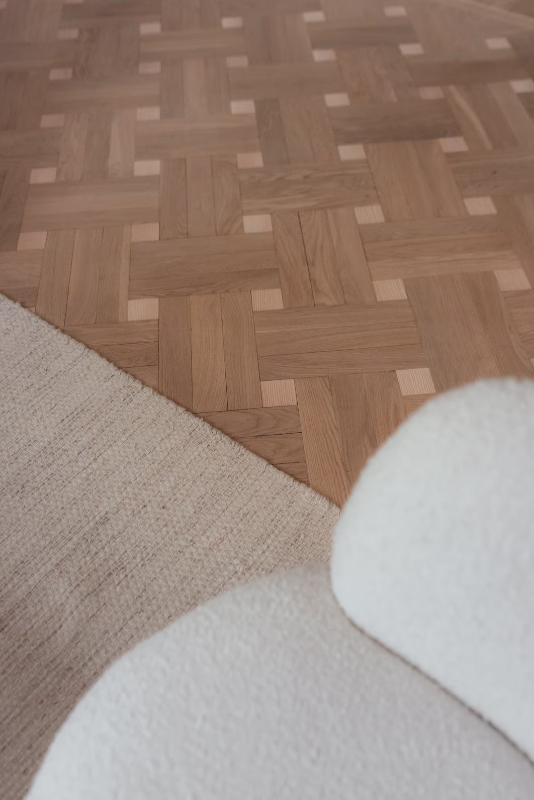 Detaljbild av fiskbensparkett och textilier som visar materialval i ett modernt mäklarkontor.