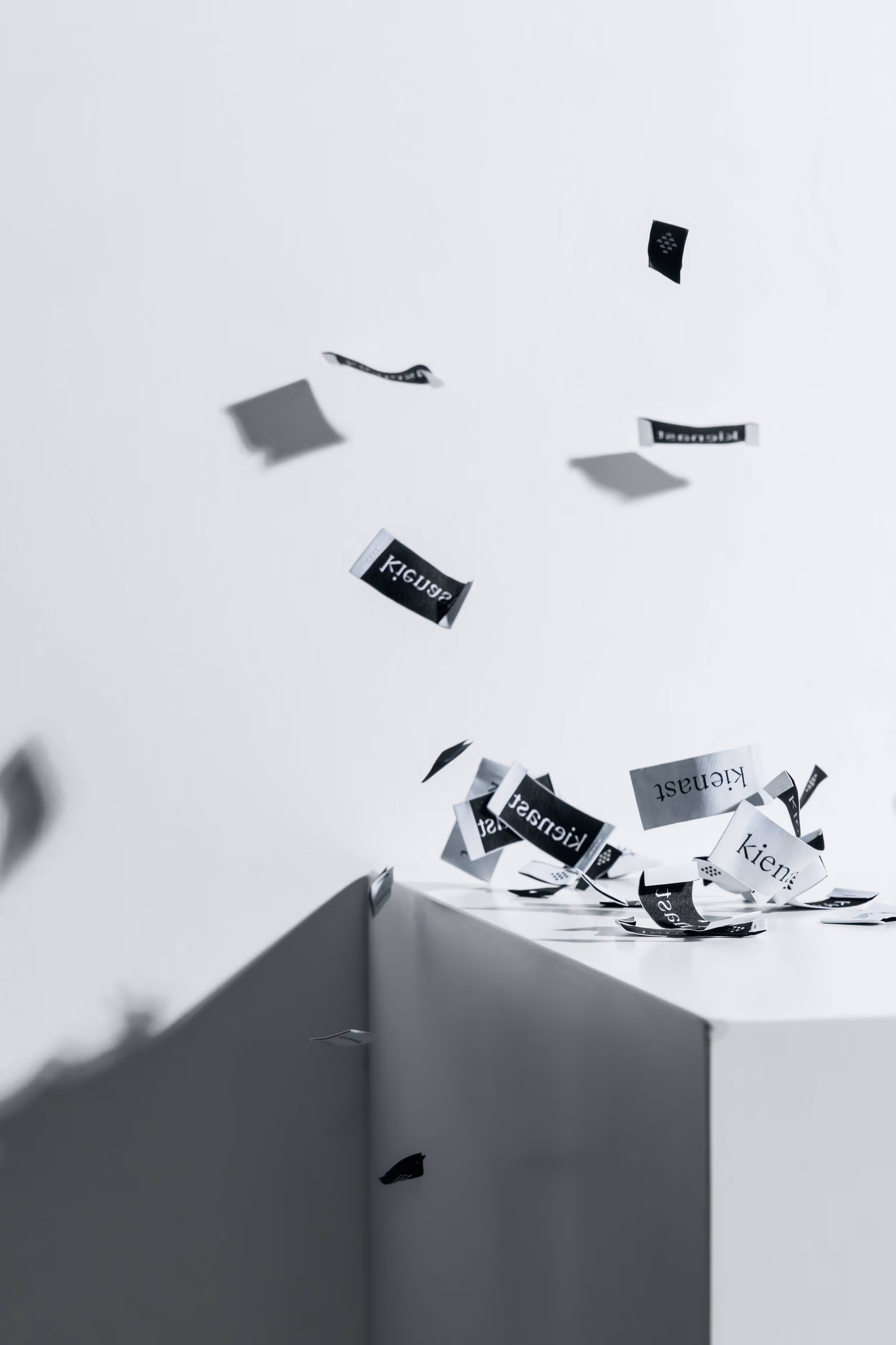 Zahlreiche, von oben nach unten fallende Stofflabels von kienast, im Hintergrund ein weisser Kubus