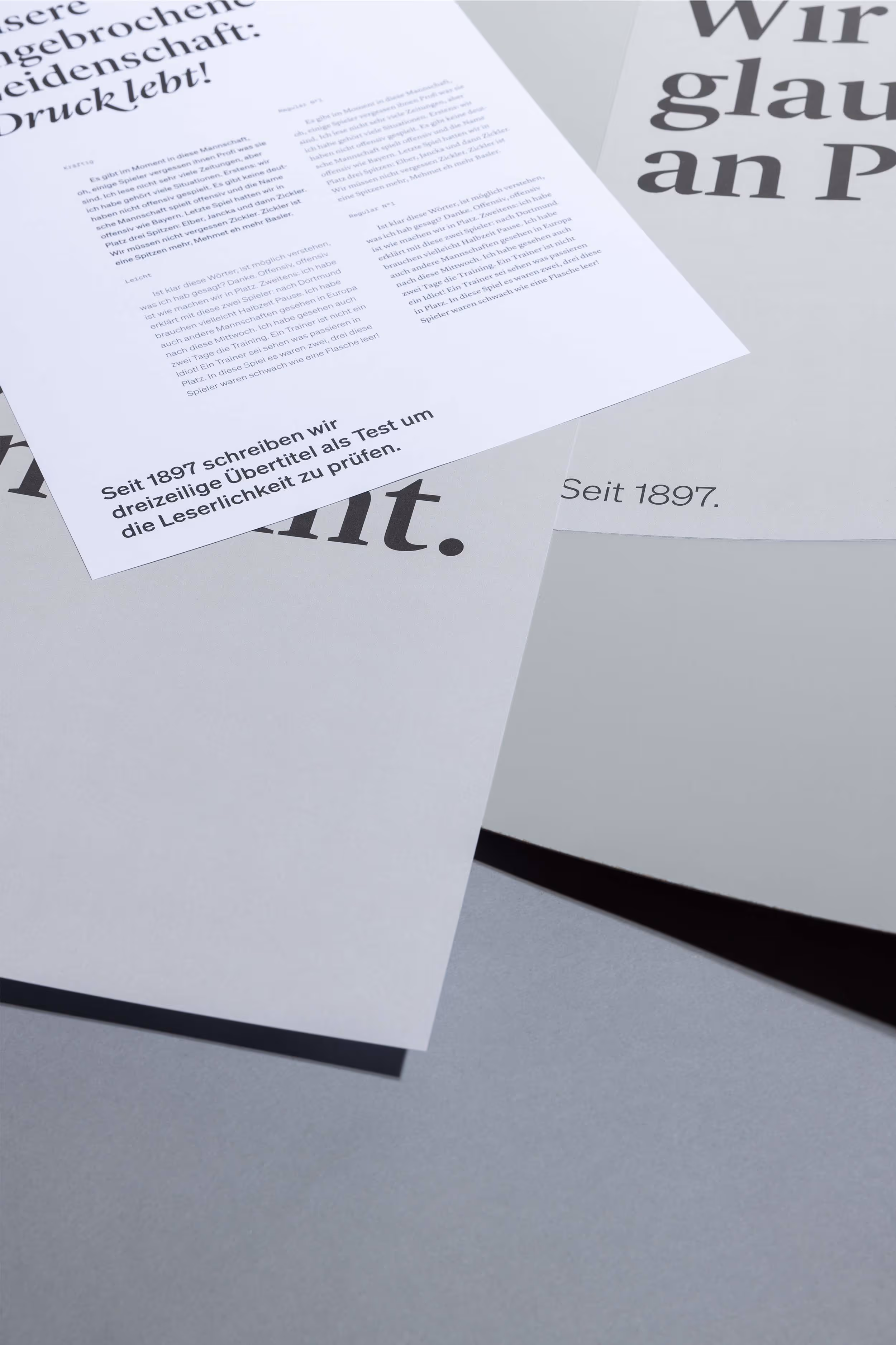 Papierbogen mit Schrift- und Farbtests für Jordi AG, wild übereinander liegend auf grauem Hintergrund