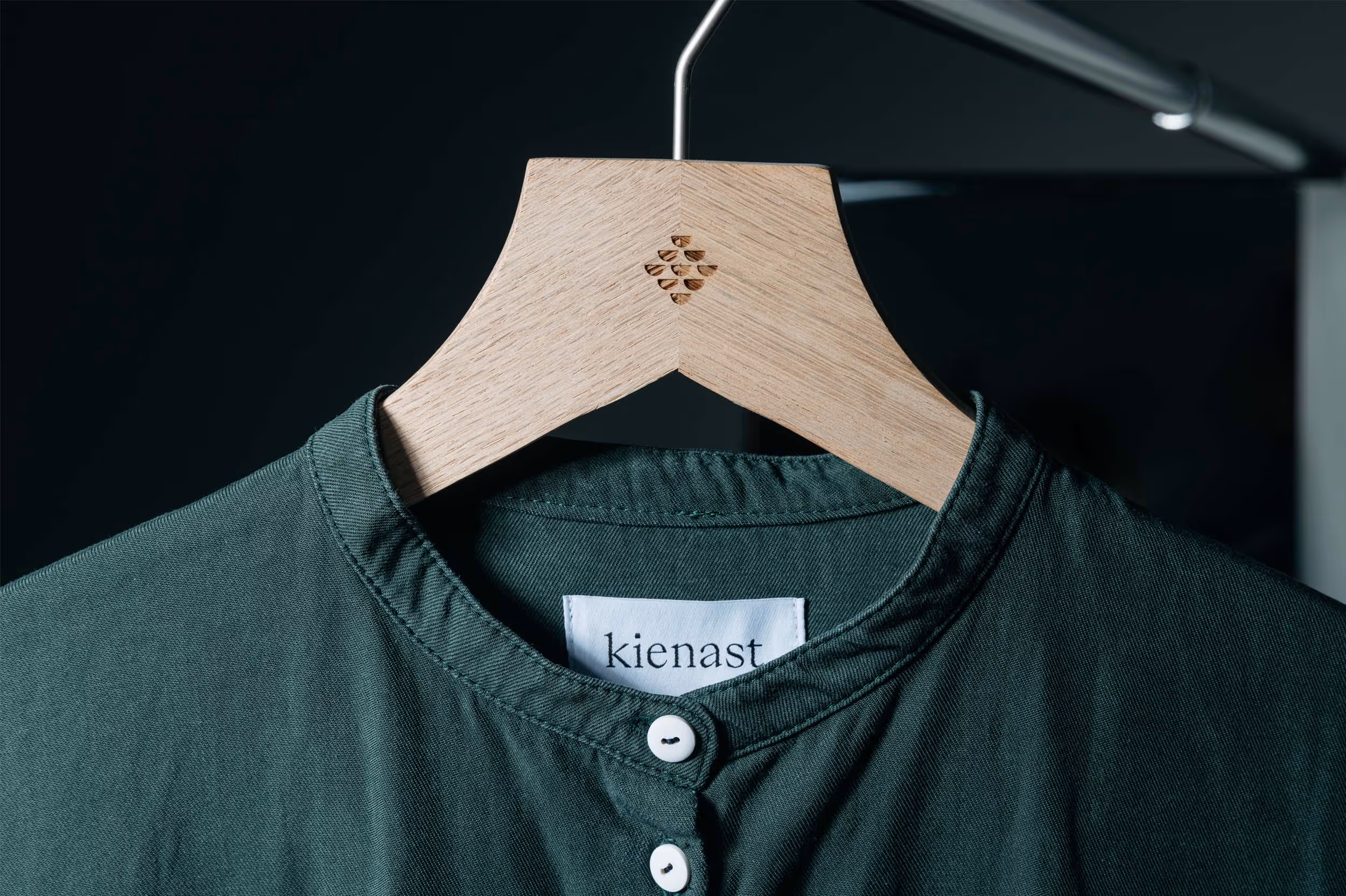 Auf Holzkleiderbügel gehängte, dunkelgrüne Blouse mit eingenähter Etikette des Modelabels kienast