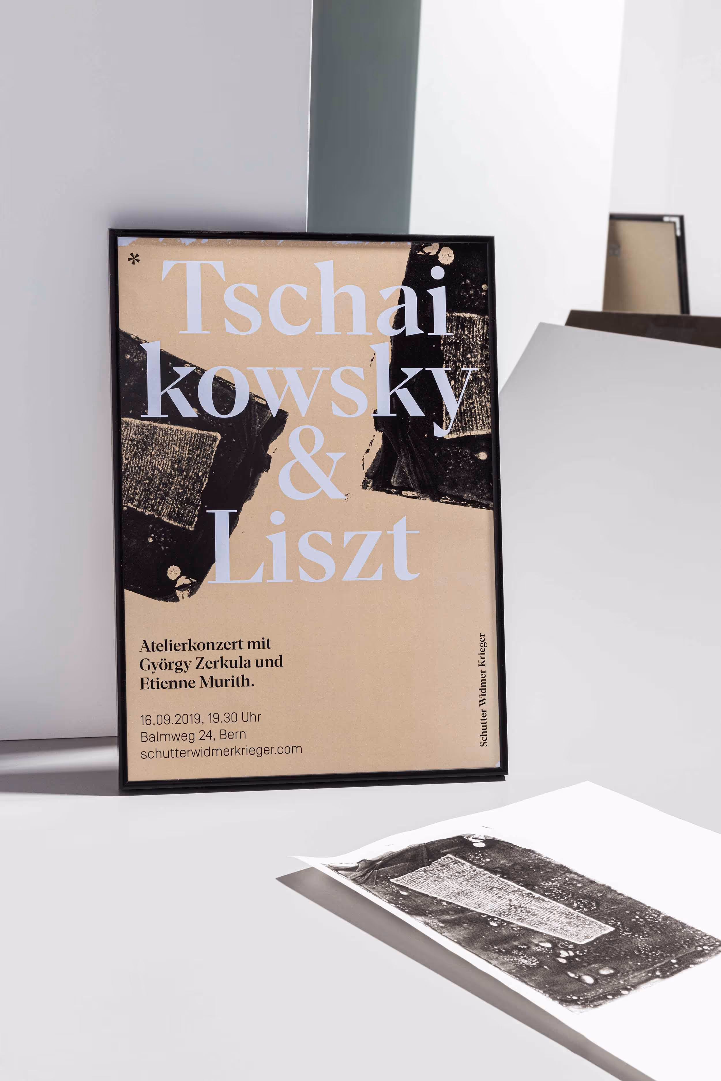 Schwarz gerahmtes, beigefarbenes Konzertplakat für das Geigenbauatelier Schutter Widmer, daneben liegender Druck eines Holzkeils