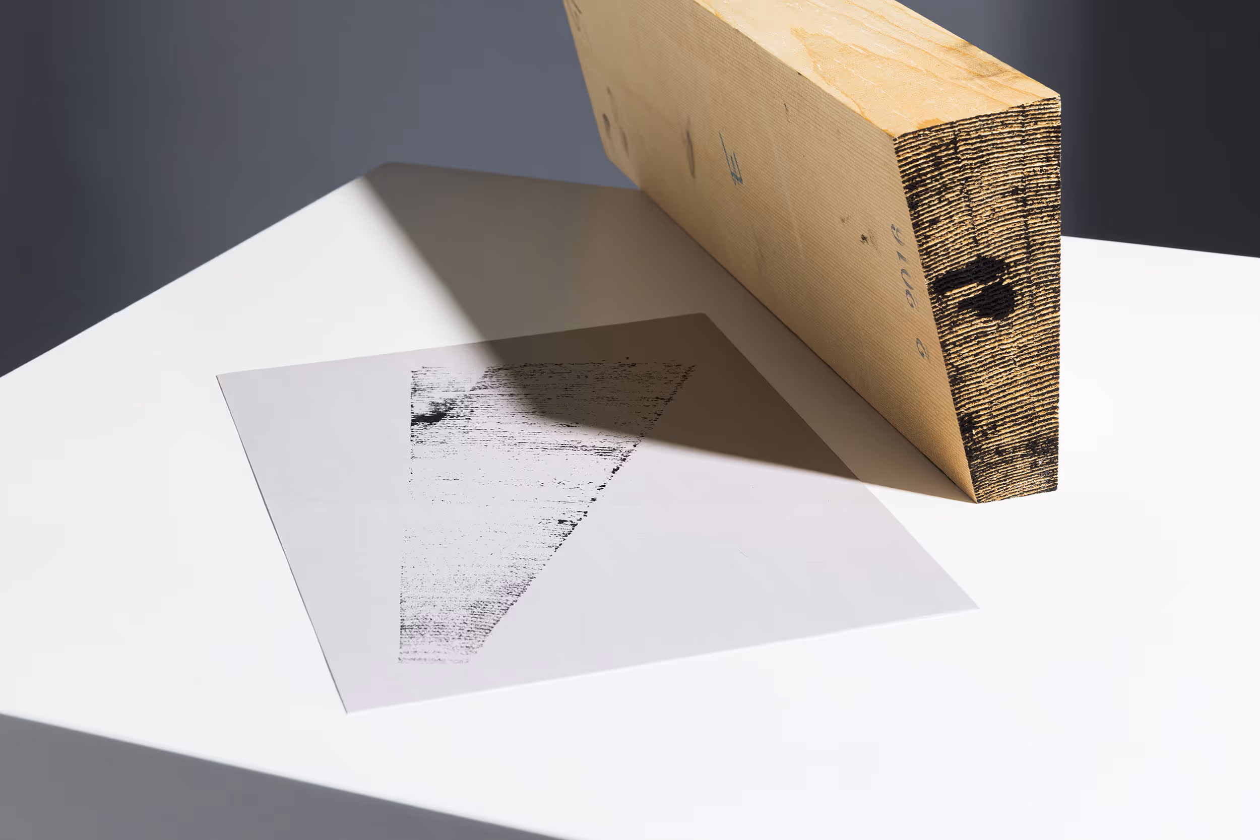 Rückseite Briefbogen mit Key Visual für das Geigenbauatelier Schutter Widmer und keilförmiges Holzstück, liegend auf weissem Kubus