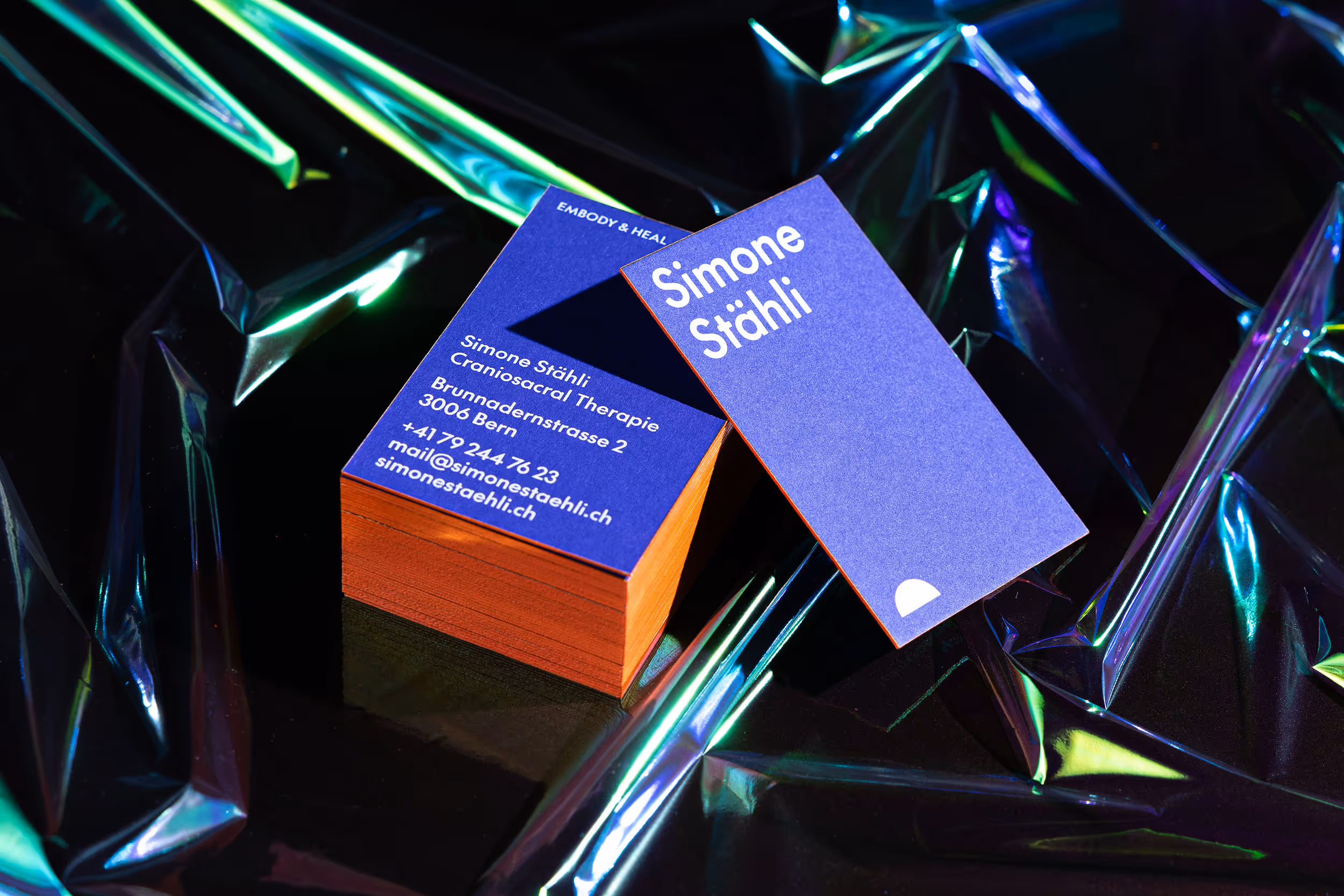 Stapel von leuchtend blauen Visitenkarten mit auffälligem, Neonorange-farbigem Farbschnitt, stehend auf dunklem Untergrund mit leuchtenden Lichtreflexen